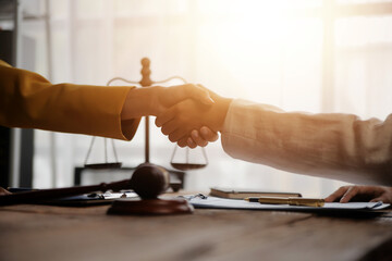 Lawyer shaking hands with a client making about documents, contracts, agreements, cooperation agreements with a female client at the lawyer's desk and a hammer at the table.