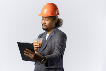 Curly haired male construction worker working using tablet while drinking a cup of coffee, construction and industry work concept, isolated on white background.