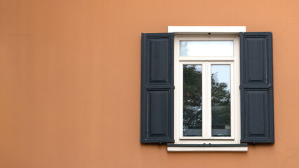 Window with wooden shutters on orange wall. Open shutter window. Exterior view of the building. Copy space.