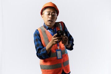 Asian adult male construction worker in full safety gear who looks very troubled carrying a smartphone and clipboard, industrial and construction concept, isolated on white background.