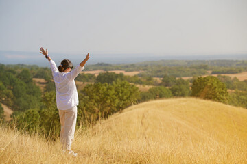 Fototapeta premium A charming girl enjoys the wind, smile and freedom, sunset and autumn light. A beautiful lady in a white dress is having fun in nature, with open arms.