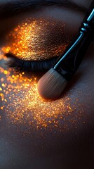 Obraz premium Close-up of a shimmering eye makeup application featuring sparkling gold tones and a makeup brush for a glamorous look.