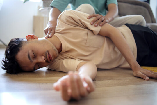 Man Doing CPR First Aid, Checking Pulse to Asian Guy at Home First Aid Emergency Rescue Concept
