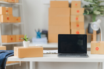 Laptop on Desk in Home Office: A clean, minimalist workspace with a laptop computer, a potted plant, and a stack of cardboard boxes in the background, a perfect image for showcasing home office, onlin
