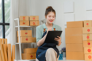 Smiling Entrepreneur Managing Orders: A young Asian woman beams with pride as she meticulously...