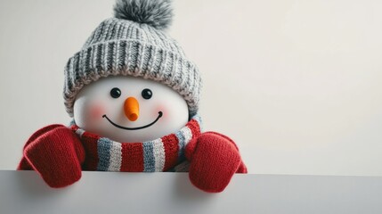 A cheerful snowman peeks over a blank surface while wearing a cozy knitted beanie and colorful scarf during a winter celebration indoors