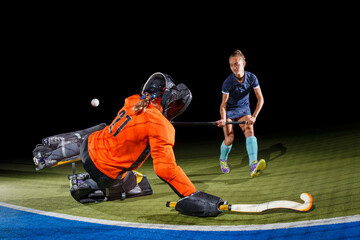 Intense field hockey action between goalkeeper and forward against black background