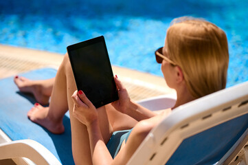 Woman using tablet computer by the pool, vertical screen mockup