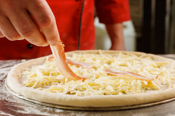 Chef adding bacon to cheese pizza