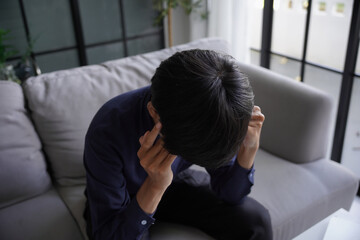 Stressed man is headache, He is sitting on sofa and massaging his head