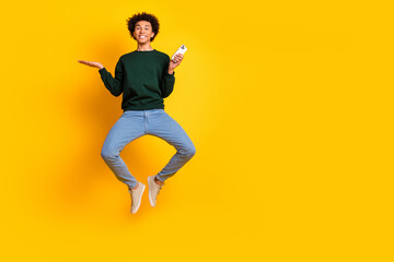 Obraz premium Full size photo of nice young man jump hold phone empty space wear pullover isolated on yellow color background