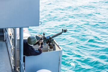 machine gun on a battleship. A marine holds a weapon. securing a ship. protection from pirates. a...
