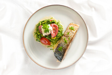 Salmon roasted with skin, vegetables from spinach and tomatoes with cream and parsley garnish, healthy fish dinner on a white tablecloth, high angle view from above, copy space