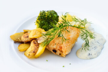 Fried fish fillet with roast potatoes, broccoli, remoulade sauce and dill garnish, served on a white plate, healthy course in a dinner menu, copy space, selected focus