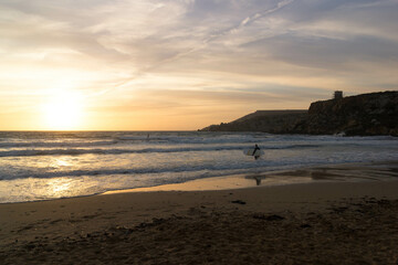 Fototapeta premium Surfer on the seashore on the beach in Melieha. Sunset in Golden Bay Malta.