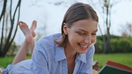 Joyful girl holding novel lying on picnic blanket at beautiful meadow closeup.