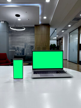 a laptop and smartphone with a green screen in a spacious office