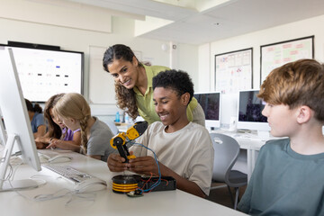 School boy showing teacher the robotic arm he is working on