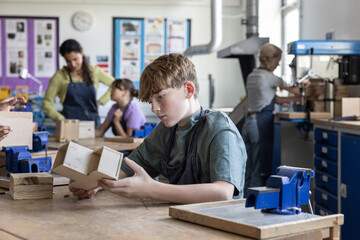Boy student looking at his project in woodworking class at school