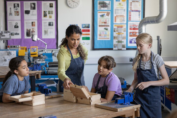 Group of girl students showing female teacher their projects in woodworking class
