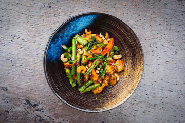 Traditional spicy chicken fillet nuggets with green asparagus, cashew nuts and broccoli in sweet sour sauce served as top view in a design bowl with text space