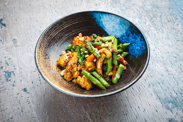 Traditional spicy chicken fillet nuggets with green asparagus, cashew nuts and broccoli in sweet sour sauce served as close-up in a design bowl with text space