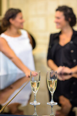 Closeup of two champagne flutes, women in background