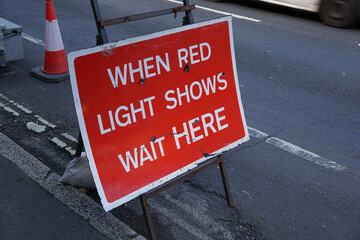Road sign at temporary traffic lights. When red light shows wait here message for motorists. Road work delays 