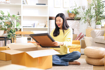 Cute asian woman is preparing a picture frame for home decoration in shopping box to send to customer who ordered online.