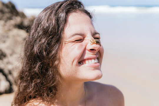 Joyful young woman with crab on face at the beach