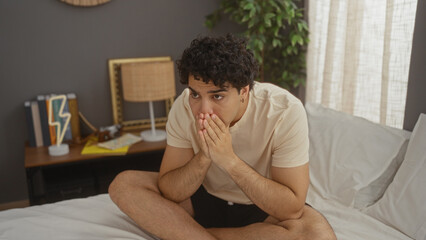 Obraz premium Handsome, young, hispanic man in contemplative pose while sitting on bed in a stylish bedroom at home.