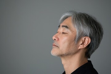 Fototapeta premium Photo of a mature, handsome Japanese man with gray hair, eyes closed in profile view on a gray background, with side lighting.generated ai