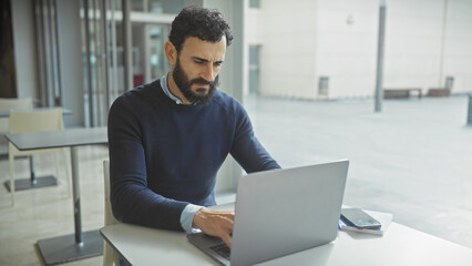 Middle-aged bearded man working on laptop in modern office space with no passport in sight