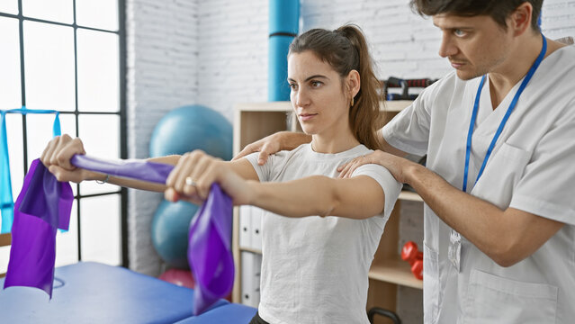 A woman patient performs physiotherapy exercises with resistance bands under the guidance of a male therapist in an indoor rehab clinic.