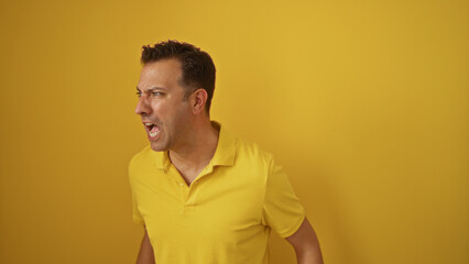 Man yelling against isolated yellow background wearing yellow polo shirt looks angry and frustrated