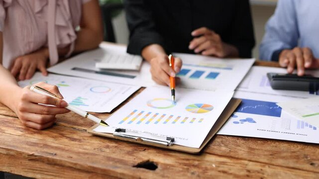Team business discussing data at meeting. Colleagues collaborating over financial documents and charts, using a calculator, at a wooden table. Brainstorming, strategy analysis and business planning.
