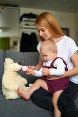 Little girl playing with mom at tea party using child. A blonde-haired mum and baby girl play tea party with a teddy bear.