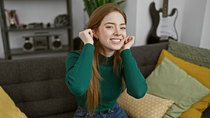 Fototapeta premium Smiling blonde woman relaxing comfortably at home on a couch with stylish pillows and guitar in the background.