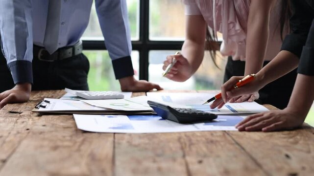 Team business discussing data at meeting. Colleagues collaborating over financial documents and charts, using a calculator, at a wooden table. Brainstorming, strategy analysis and business planning.