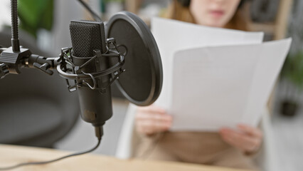Focused caucasian woman records audio in modern radio studio with professional microphone and...