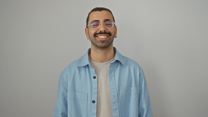 Hispanic man smiling over an isolated white background, wearing a light blue shirt and glasses, displaying a stylish moustache and an attractive appearance.