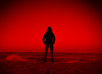 Person in silhouette contemplating on the beach by the sea in red