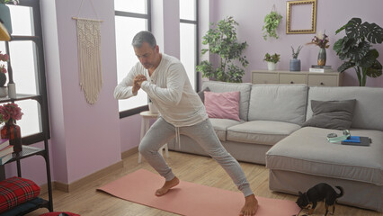 Middle-aged hispanic man exercising in a cozy living room indoors with a small chihuahua dog nearby.