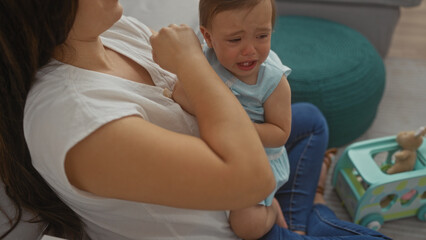 Woman comforting crying infant in living room, showcasing bonding, mother soothing daughter in cozy home interior during day.