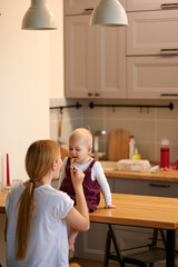 Mother feeding her baby. Baby girl mimicking mother whilst eating at kitchen table. Mother brought the spoonful of oud to the little girl's mouth.
