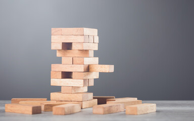 Precarious stack of wooden blocks towers on the table against a grey wall background. Symbolizes risk, uncertainty, and careful decision-making, much like in a game of balancing strategy and chance