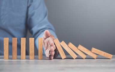 Businessman uses his hand stopping wooden blocks from falling, representing the domino effect and risk management. Symbolizes taking action to prevent cascading problems and managing risks effectively