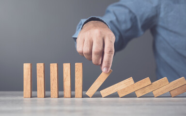 Businessman uses his hand stopping wooden blocks from falling, representing the domino effect and risk management. Symbolizes taking action to prevent cascading problems and managing risks effectively