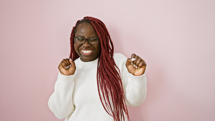 Joyful african woman with braids wearing glasses and white sweater dancing over pink background