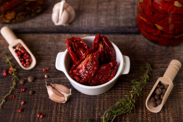 Sun-dried tomatoes in olive oil in a white bowl with pepper, garlic and thyme in a rustic style. Selective focus, close-up.